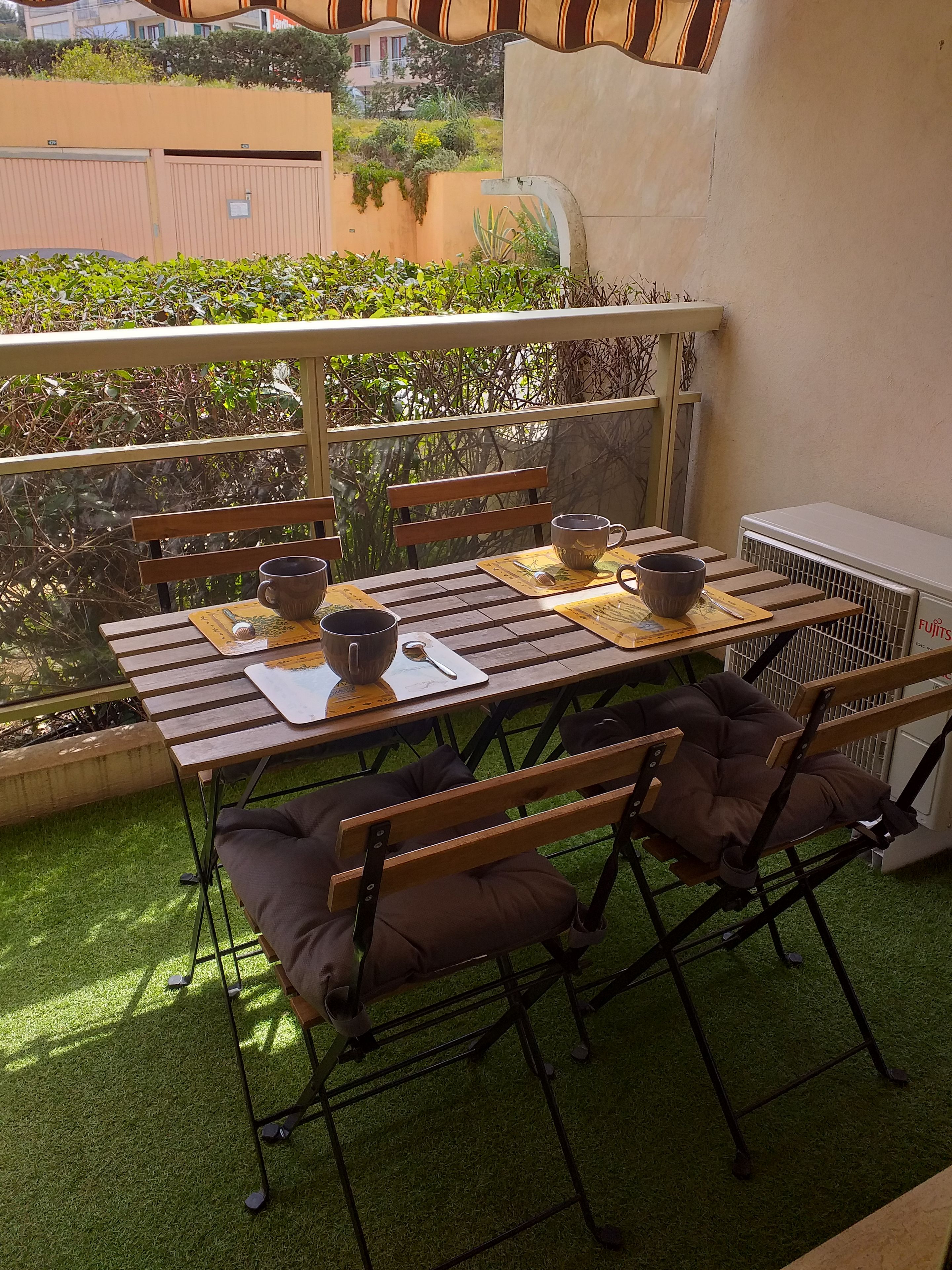 Une table en bois avec des chaises, un banc et un radiateur sur un balcon recouvert de gazon synthétique.