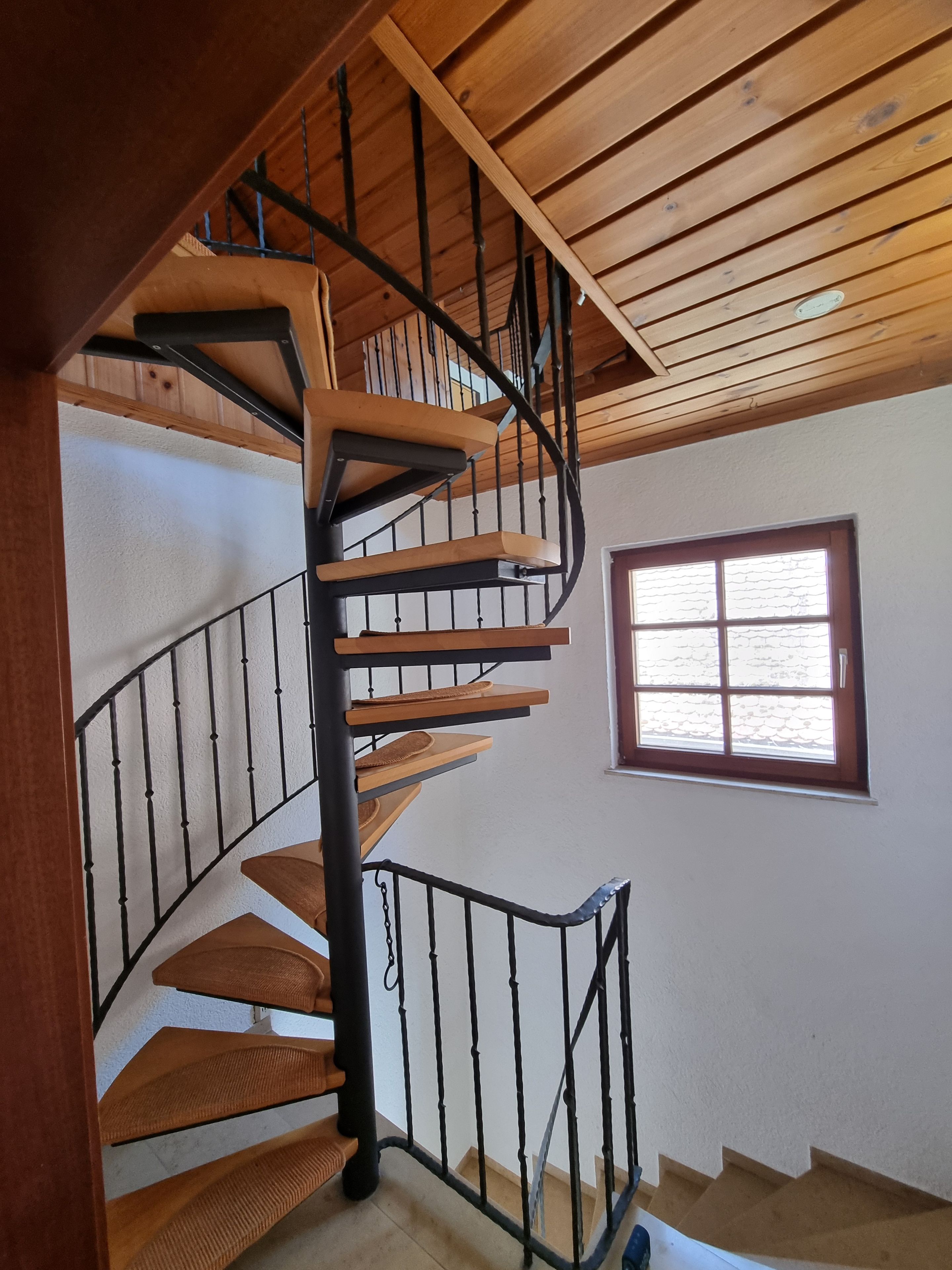 Eine Wendeltreppe mit Holzbodenstufen und schwarzen Geländern, die zu einer oberen Etage führt.