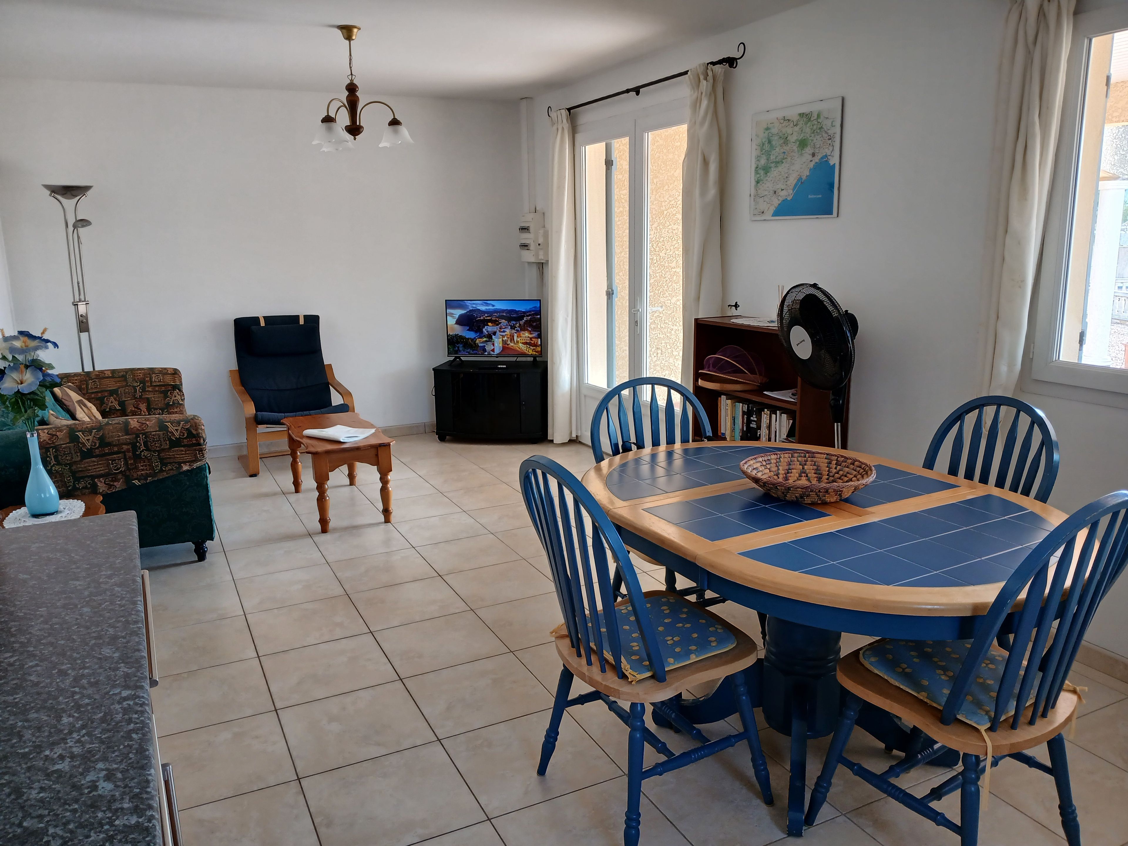 Un comedor con una mesa redonda, sillas azules, un televisor y una estantería.