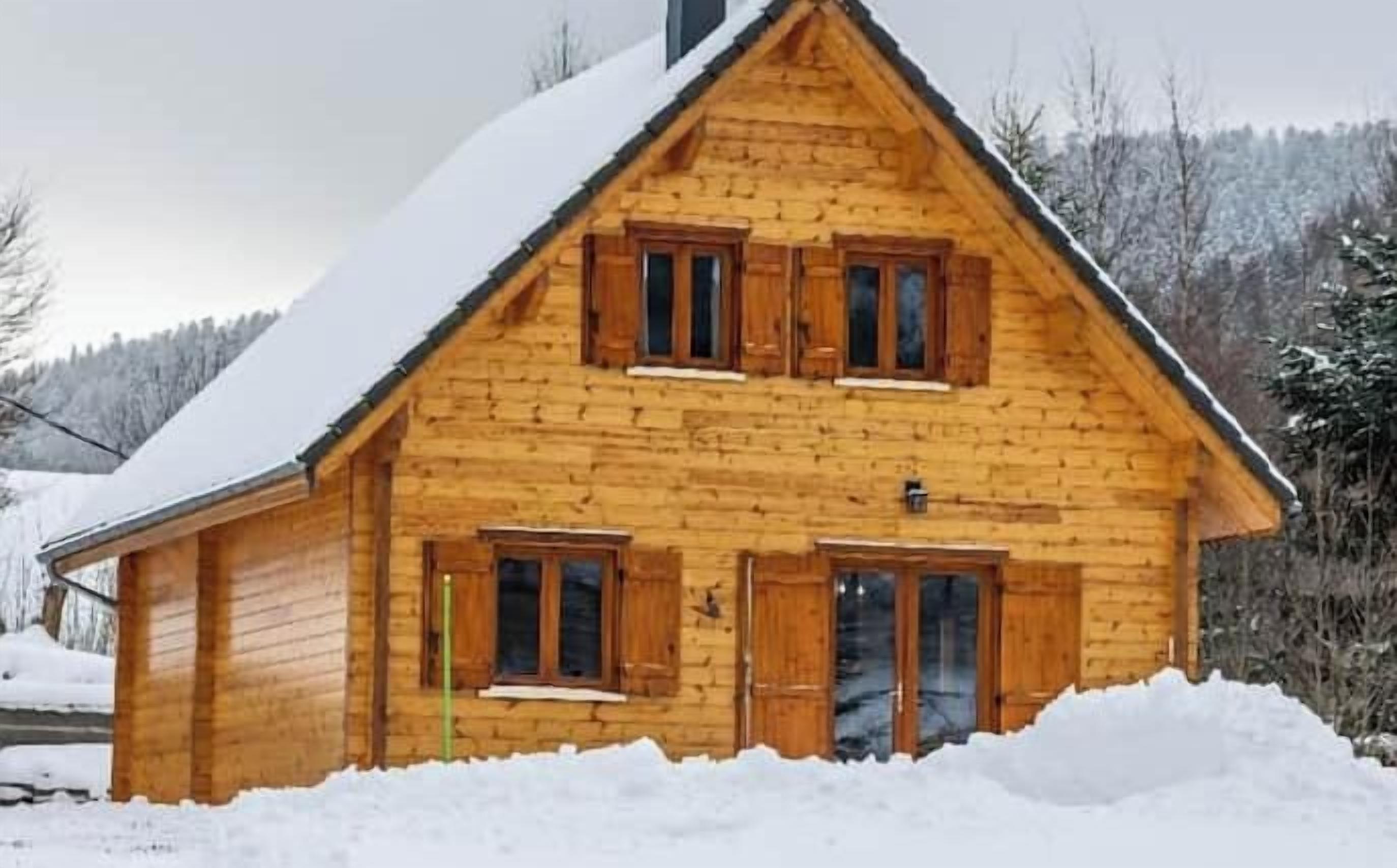 A wooden cabin with a steeply pitched roof, a front porch, and a chimney.