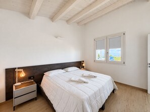 Ein Schlafzimmer mit Bett, Nachttischen, einem Fenster mit Blick und Holzbalken an der Decke.