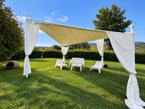 Ein Außenbereich mit Markise, zwei weiße Stühle und ein kleiner Tisch.