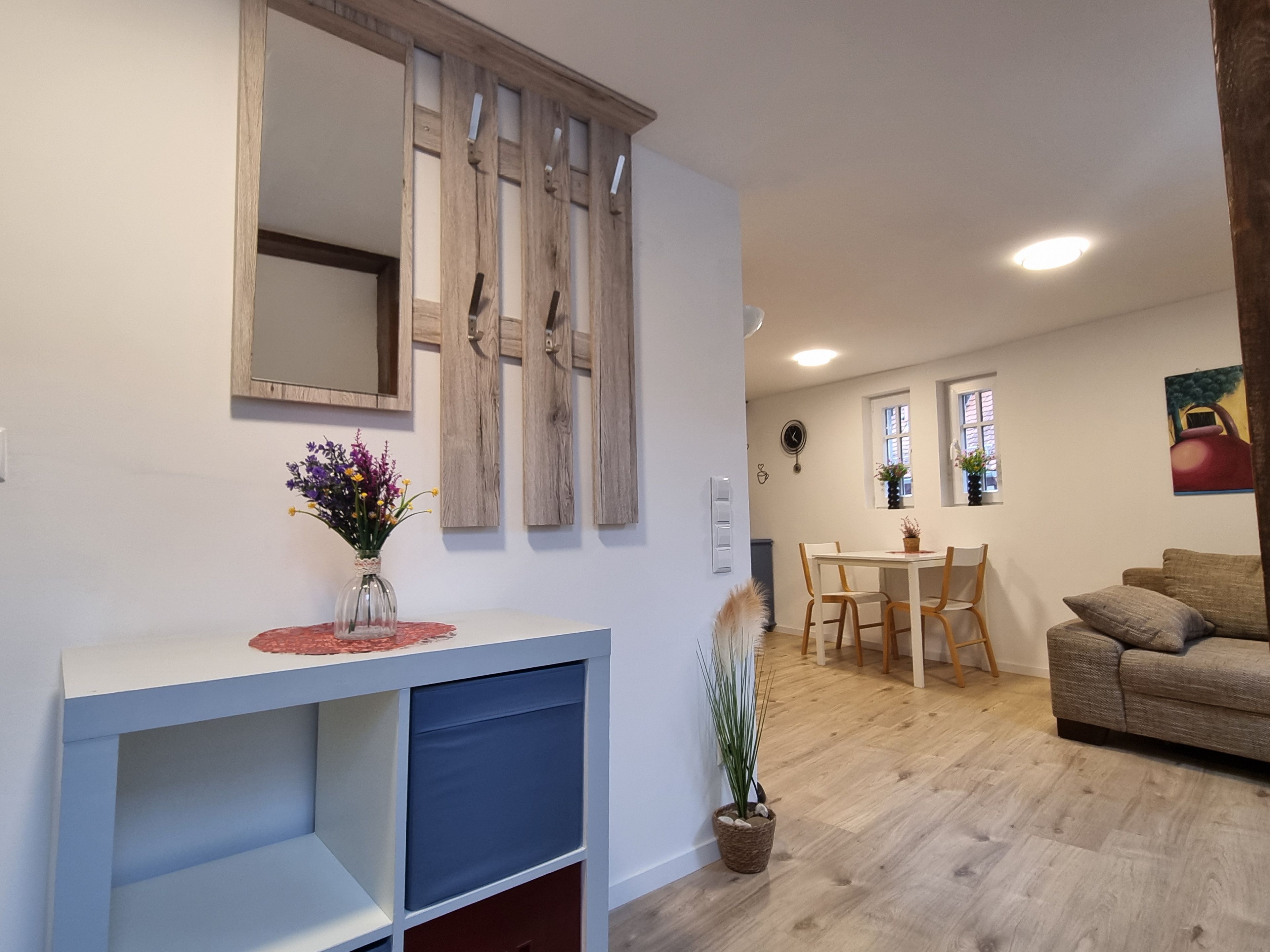 A modern living room with a white console table, a sofa, and a dining area with wooden chairs and a table.