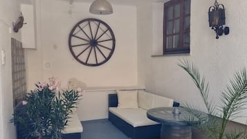 Ein überdachter Außenbereich mit Sitzgelegenheiten, einer runden Wanddekoration, einem Fenster und Topfpflanzen.