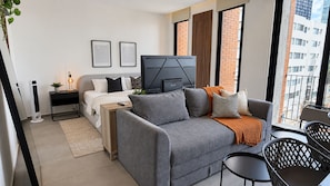 A modern bedroom with a grey sofa, a bed, a TV, and a balcony with a view of buildings. - Modern Providencia Loft with Pool, Gym & Coworking (Guadalajara)