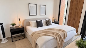 A modern bedroom with a bed, bedside tables, a wall-mounted light, and a view of a brick building. - Modern Providencia Loft with Pool, Gym & Coworking (Guadalajara)