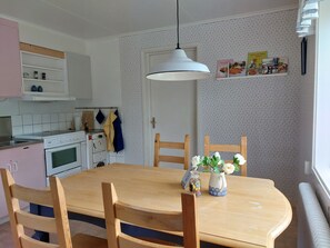 Keittiössä on ruokapöytä, tuoleja, riippuvalaisin sekä seinälle kiinnitetty hylly, jossa on ruokakirjoja.