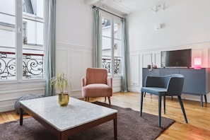 A modern living room with a marble coffee table, a pink armchair, a blue armchair, and a grey cabinet with a TV. - Lovely Flat near Notre-Dame & Le Marais (Paris)