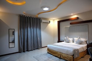 A modern bedroom with a bed, curtains, an air conditioning unit, a mirror, and a headboard with patterned pillows. - Quiet room 15 (riyadh)