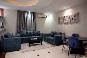 A modern living room with a sectional sofa, a coffee table, and a dining area with a chair. - Quiet room 15 (riyadh)