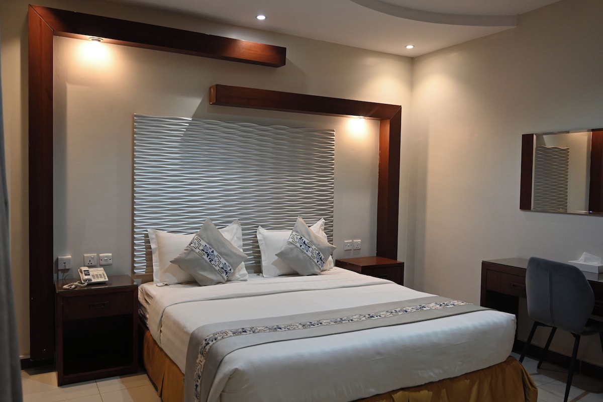 A hotel room with a large bed, bedside tables, a desk, and a chair.