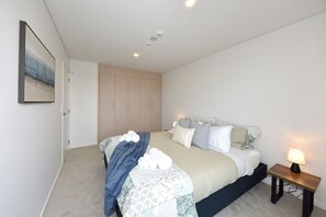 Un dormitorio con una cama, una mesita de noche con lámpara, un armario y un cuadro en la pared.