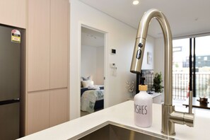 Eine moderne Küche mit einem Edelstahlarmaturen, einer weißen Arbeitsplatte und einer mit 'DISHES' beschrifteten Flasche.