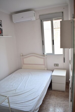 A bedroom with a single bed, a bedside table, a nightstand, an air conditioning unit, and a window. - New Listing (Madrid)
