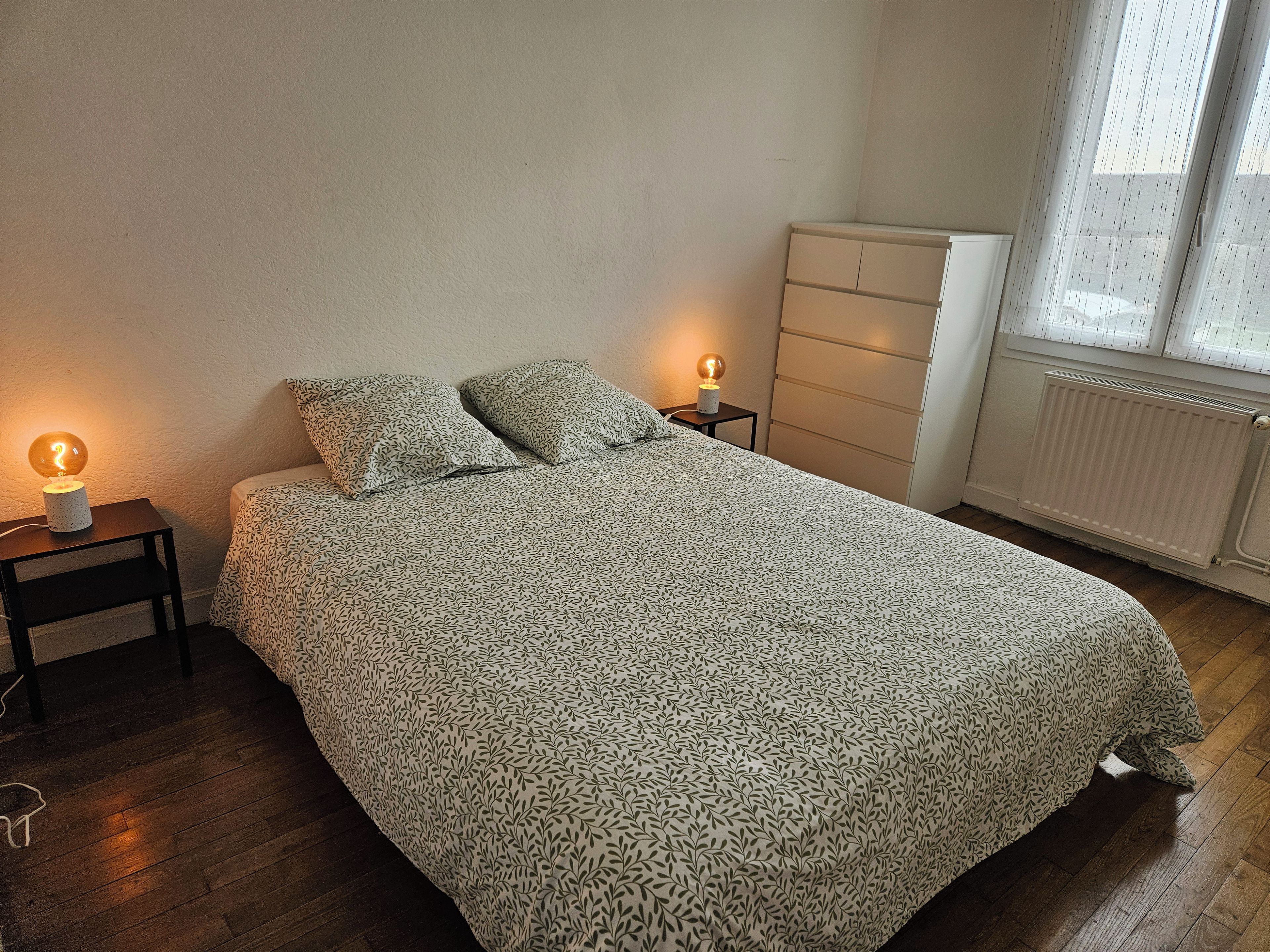 Een slaapkamer met een bed, twee bedlampen, een dressoir en een radiator.