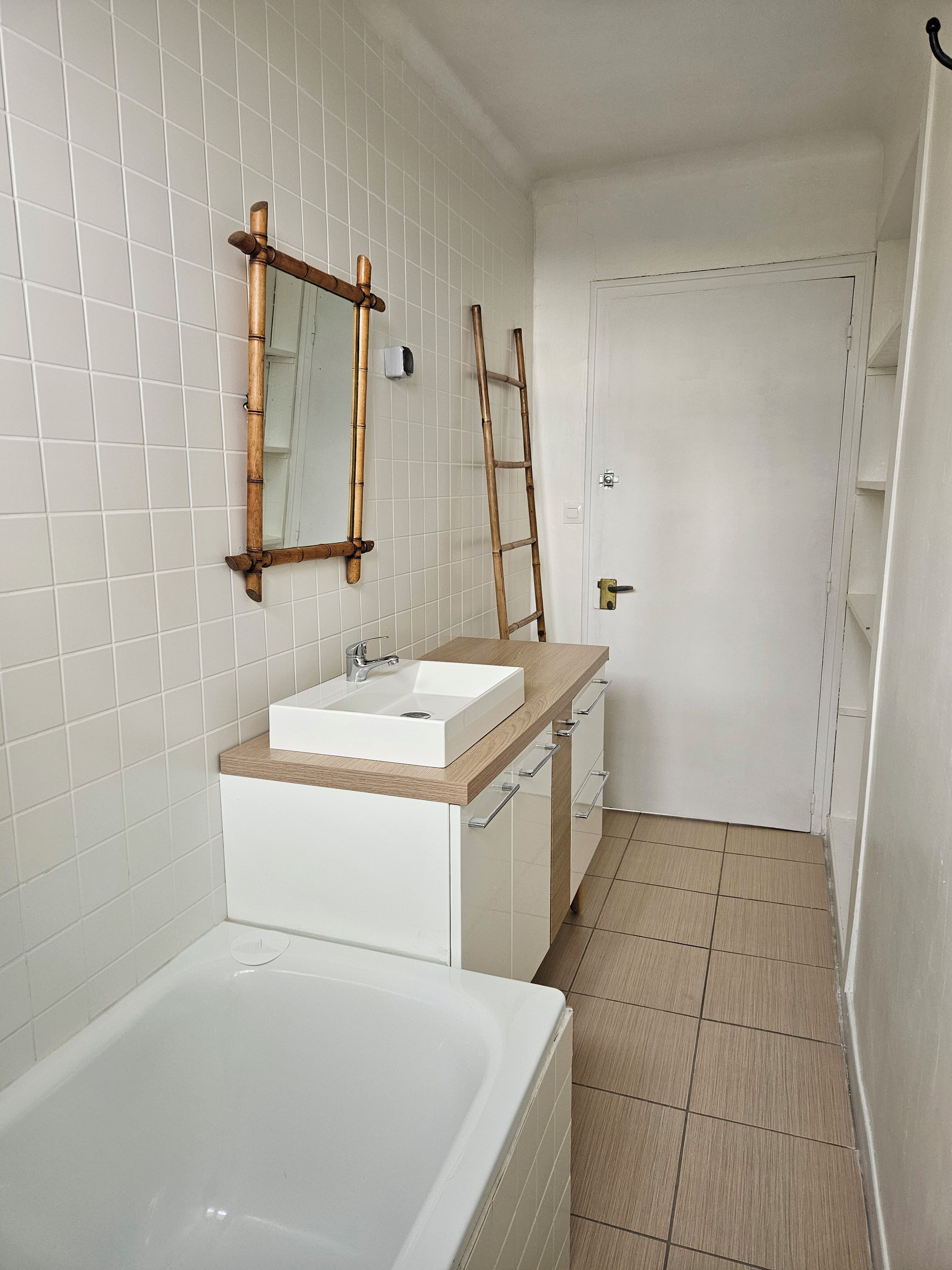 A bathroom with a white bathtub, a wooden vanity with a sink, and a mirror.