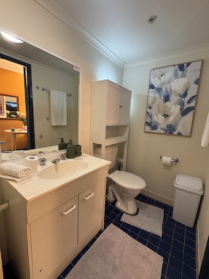 Ein Badezimmer mit weißem Waschbecken, Spiegel und Schrank, einer Toilette und blau gefliestem Boden.
