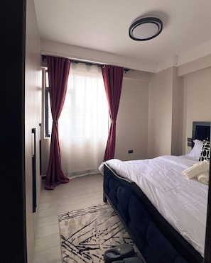 A hotel room with a bed, a window with curtains, a door, and a ceiling light. - Homely • Stylish • Afro-Modern • Vibrant (Nairobi)