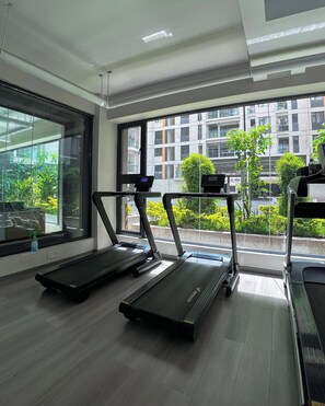 Ein Fitnessstudio mit Laufbändern, großen Fenstern und Blick auf eine Stadtlandschaft.