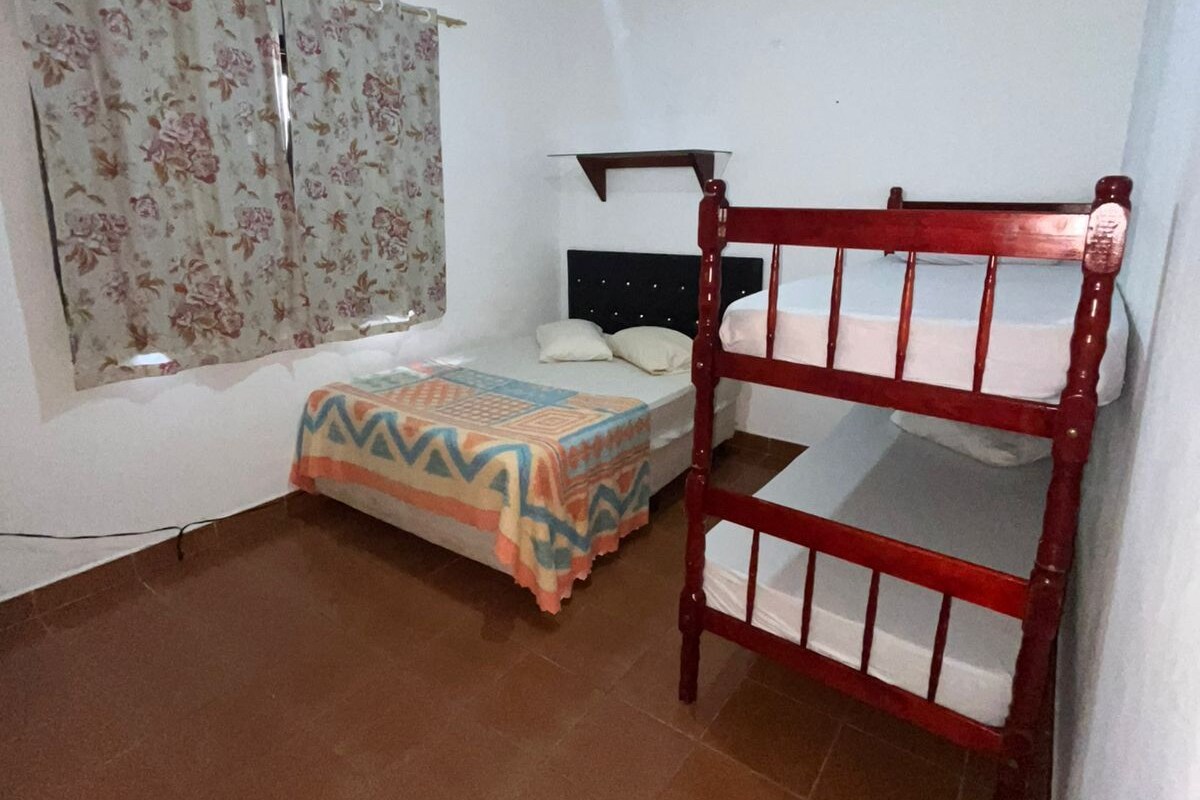 A room with a bunk bed, a single bed, a ceiling fan, and a window with curtains.