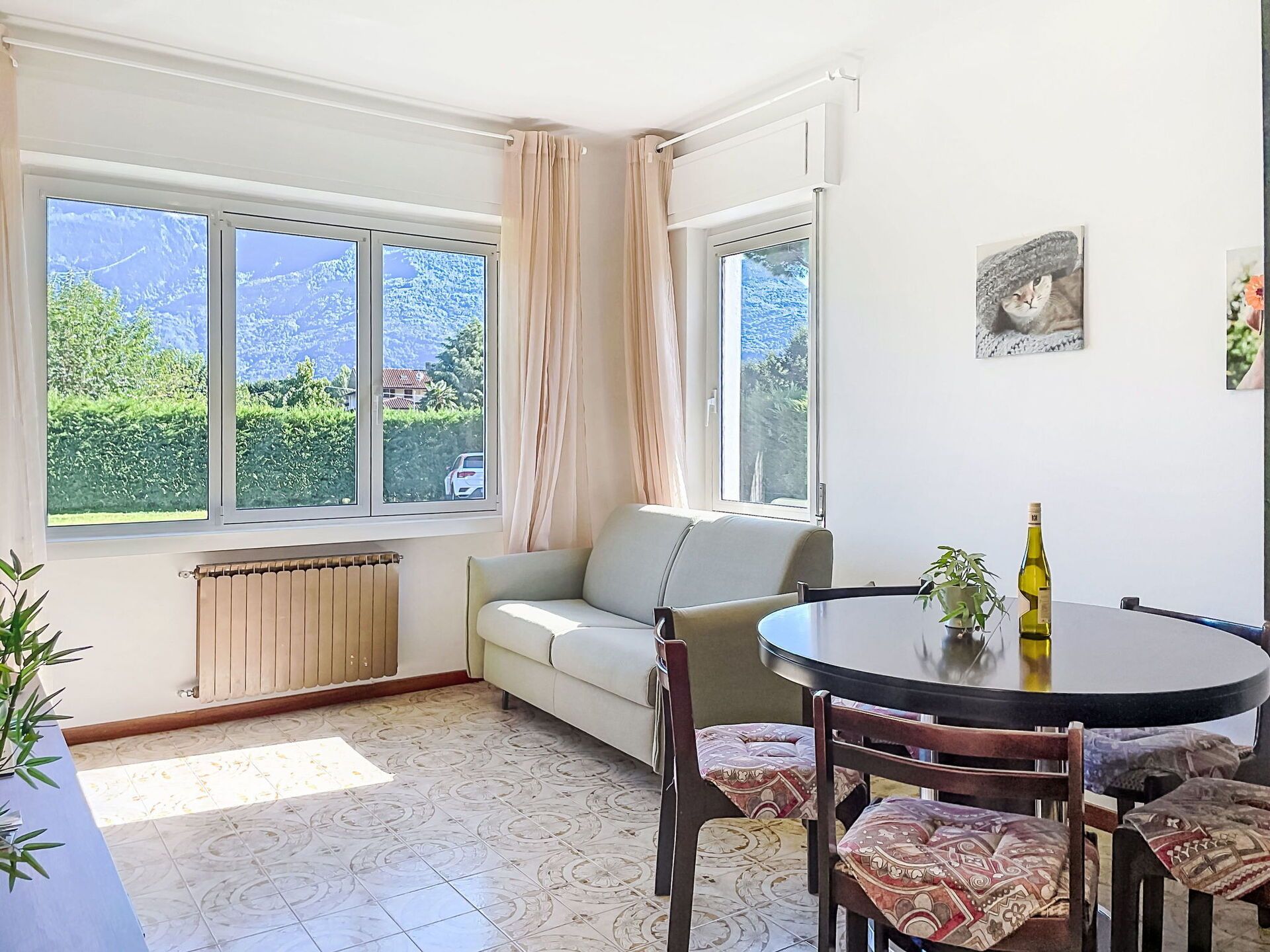 A room with a sofa, a dining table with chairs, a radiator, and a window with curtains.