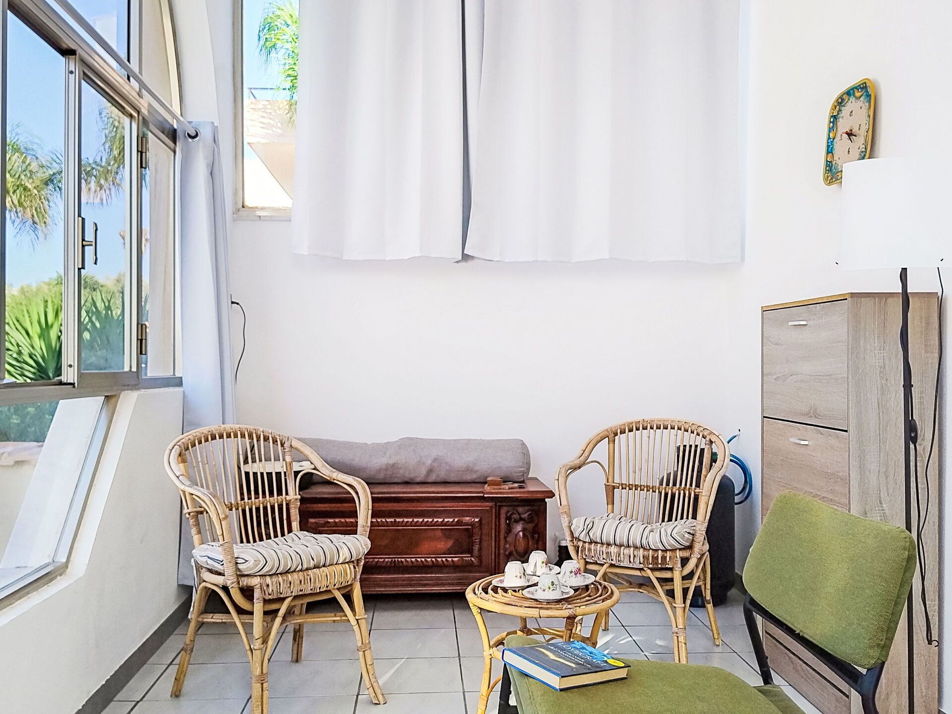 Un balcon agrémenté de meubles en osier, d’un canapé, d’une petite table avec des tasses et d’une chaise verte.