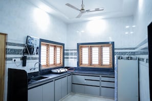 A compact kitchen with a gas stove, a built-in oven, and a ceiling fan. - StayGuru Kutch Shahi Haveli (Bhuj)