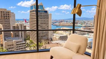 A room with a large window offering a city view, a beige armchair, and a floor lamp.