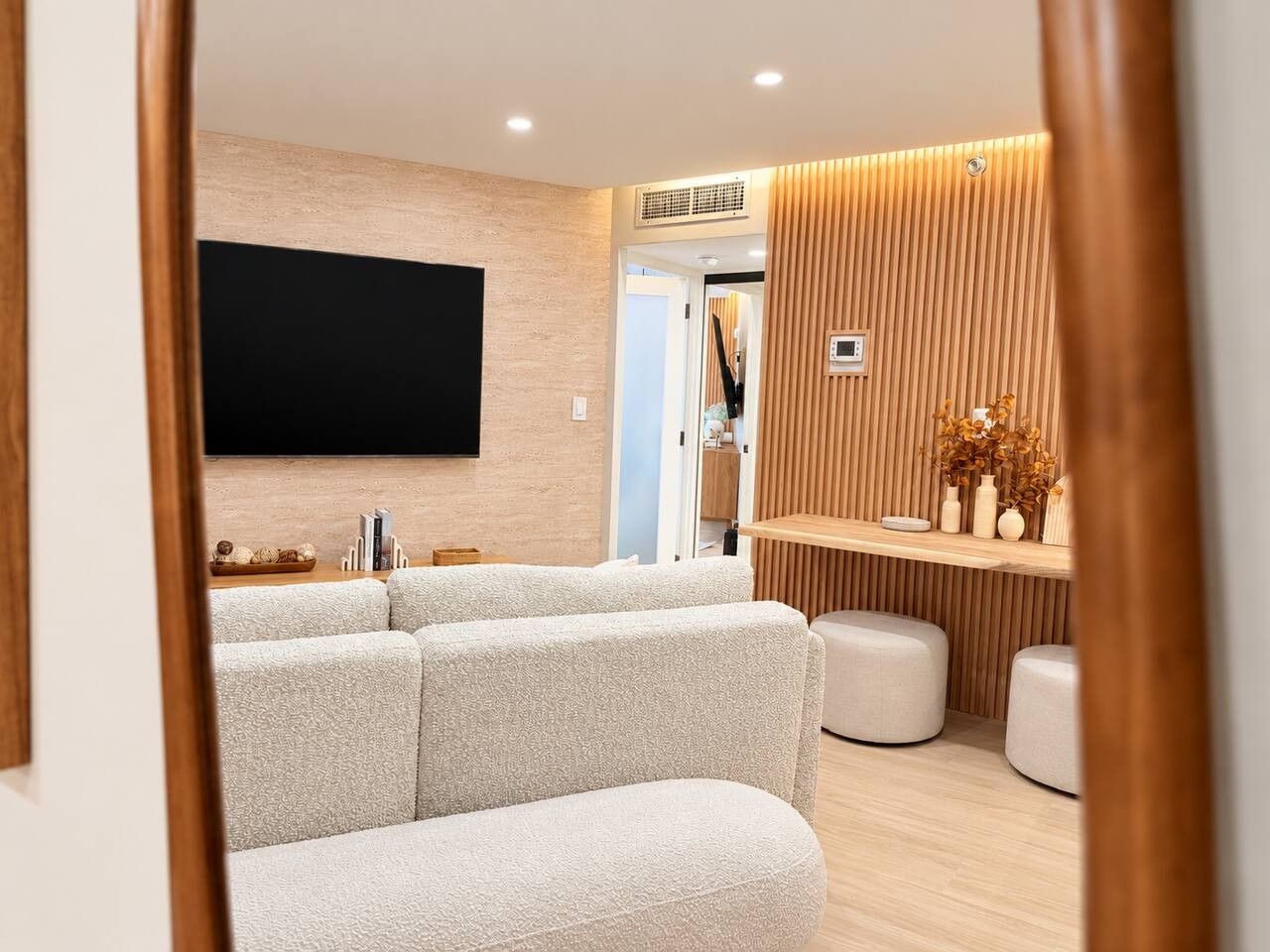 A modern living room with a flat-screen TV, a sofa, ottomans, and a wooden accent wall.