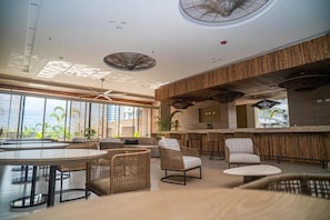 A modern lounge area with wicker furniture, a bar, and large windows offering a view of the city. - Stunning Oceanfront Condo in Santa Marta Sleeps 5 + Resort Amenities (BELLO HORIZONTE)