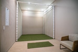 A room with a netted play area, a green artificial turf, a wicker sofa, and a light switch on the wall. - Stunning Oceanfront Condo in Santa Marta Sleeps 5 + Resort Amenities (BELLO HORIZONTE)