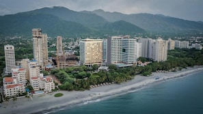 Een kuststadsgezicht met wolkenkrabbers, een strand en bergen op de achtergrond.