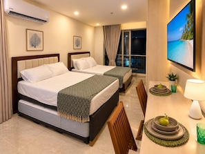 Ein Hotelzimmer mit zwei Betten, einem Esstisch mit Stühlen, einem Fernseher und einem Balkon mit Vorhängen.