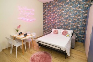 A bedroom with a bed, a small table with chairs, a neon sign, and a floral wallpaper. - New Listing (Napoli)