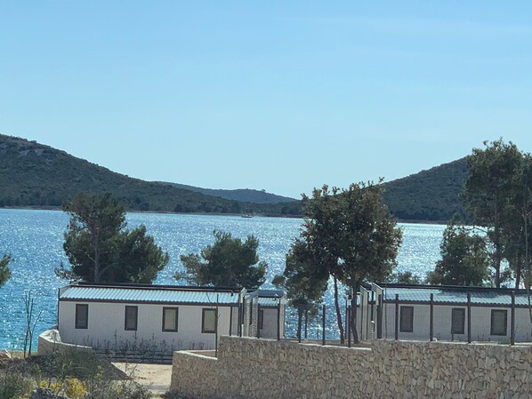 A coastal building with a stone wall in the foreground, a body of water, and hills in the background.