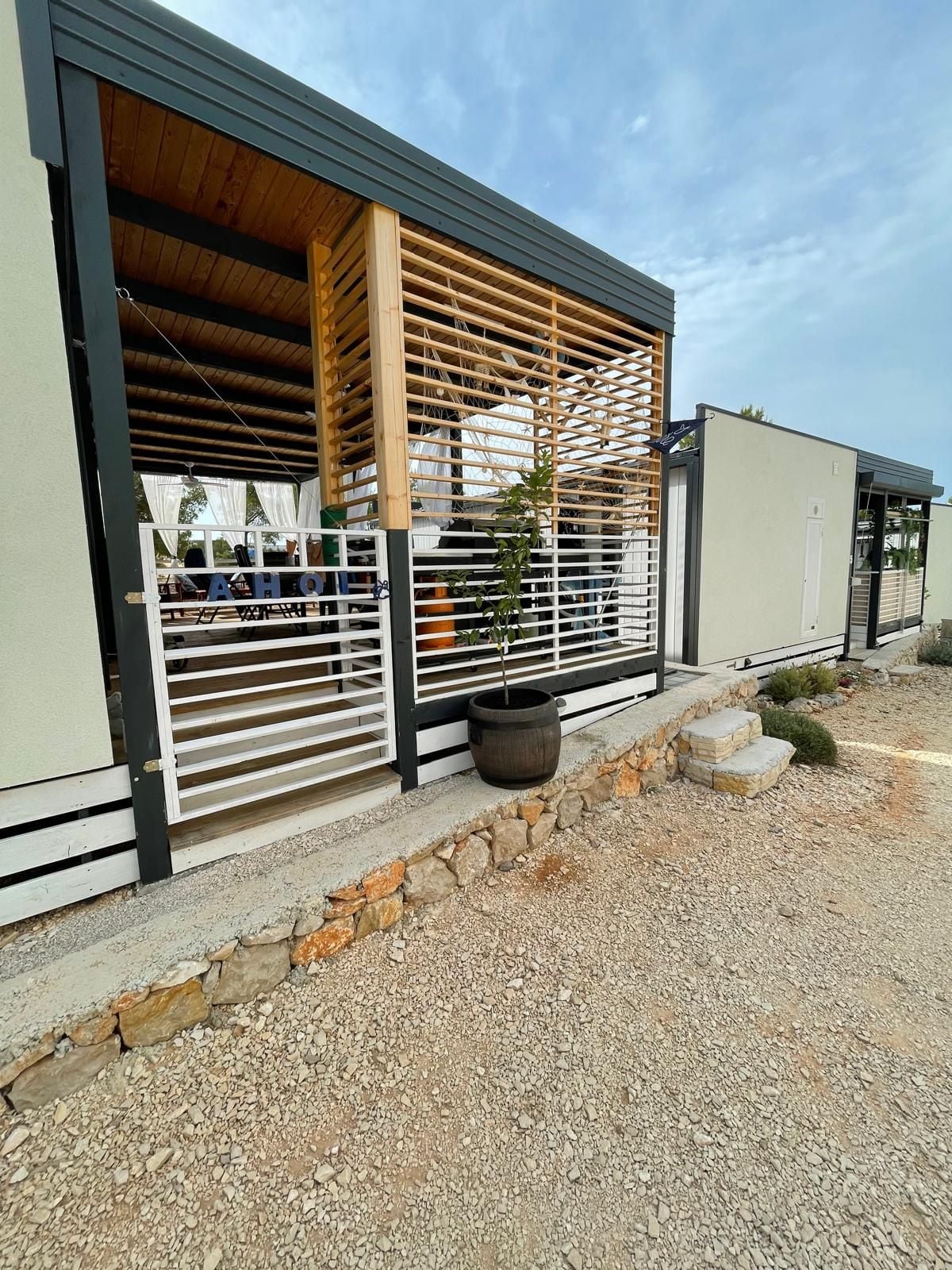 A modern building with a wooden slatted facade, a stone retaining wall, and a potted plant.