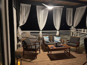 An outdoor deck with wooden furniture, white curtains, and a ceiling fan. - Ahoi House 7 – Seaside mobile home in Drage, sleeps 6 (Drage)