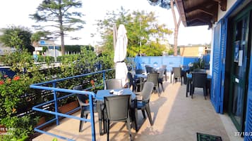 Ein Außenbereich mit Terrasse, Tischen, Stühlen, einem blauen Geländer und Pflanzen in Töpfen.