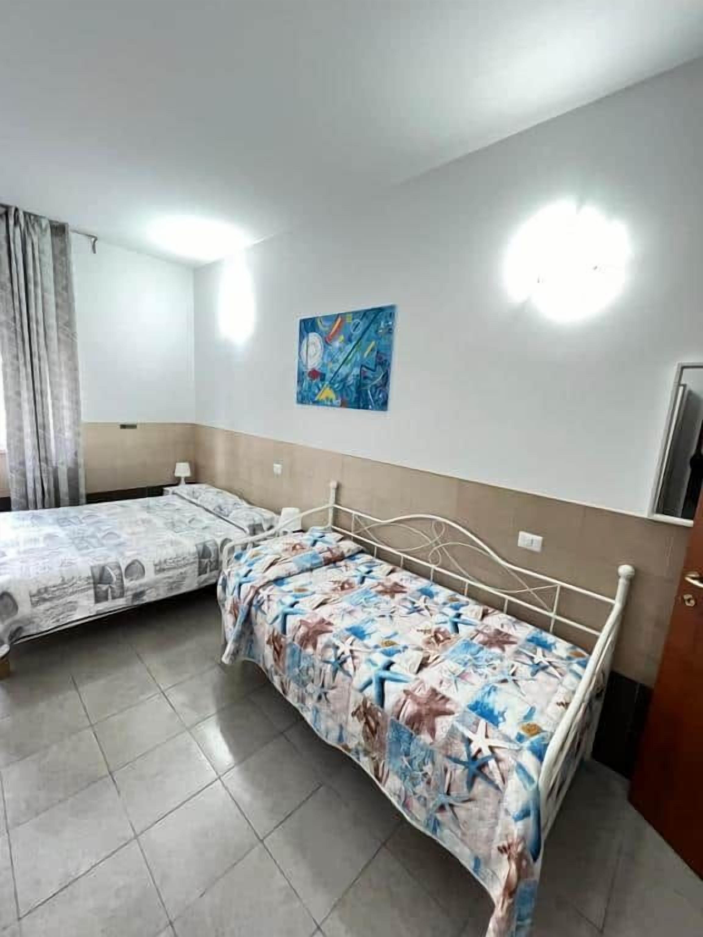 Une chambre avec deux lits, une œuvre d’art accrochée au mur et un luminaire au plafond.
