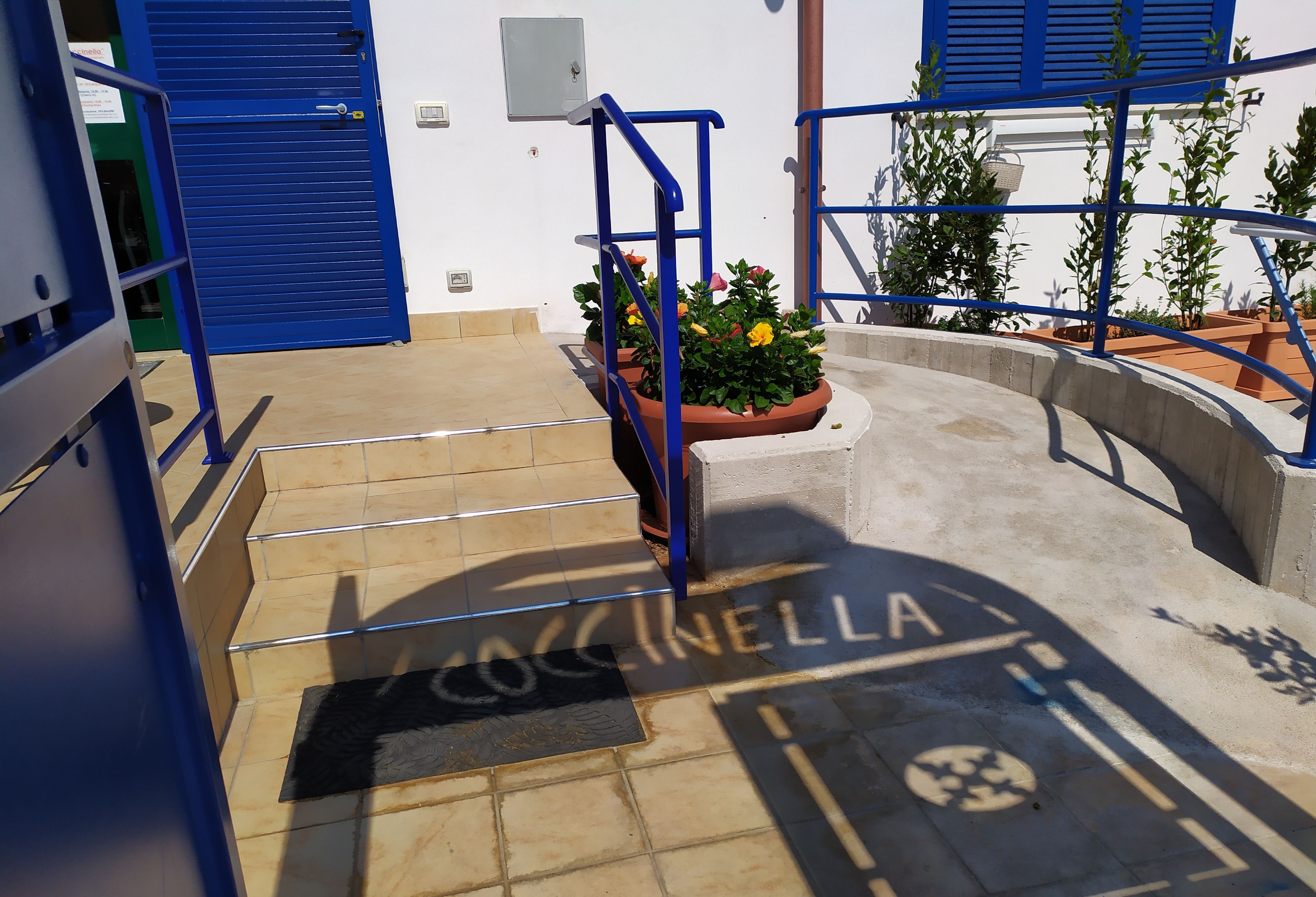 A set of outdoor stairs leading to a building entrance with a blue door and a sign reading 'Cocinella'.