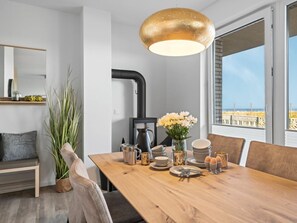 Ein Essbereich mit Holztisch, Stühlen, einem Blumenstrauß und Blick auf den Strand durch große Fenster.