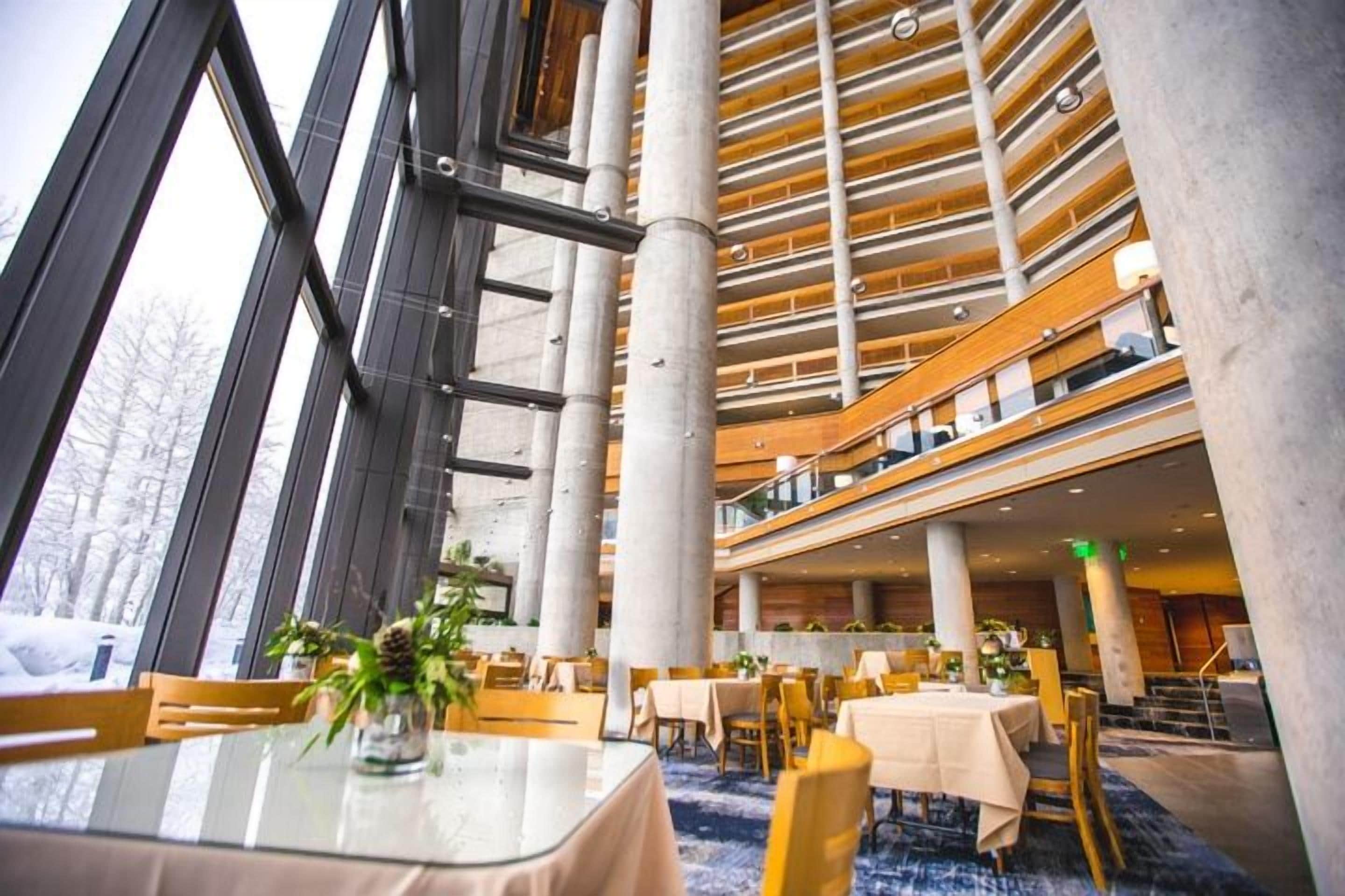 Un hall d’hôtel à plusieurs niveaux, doté de murs en verre, de poutres en bois et d’un atrium central.