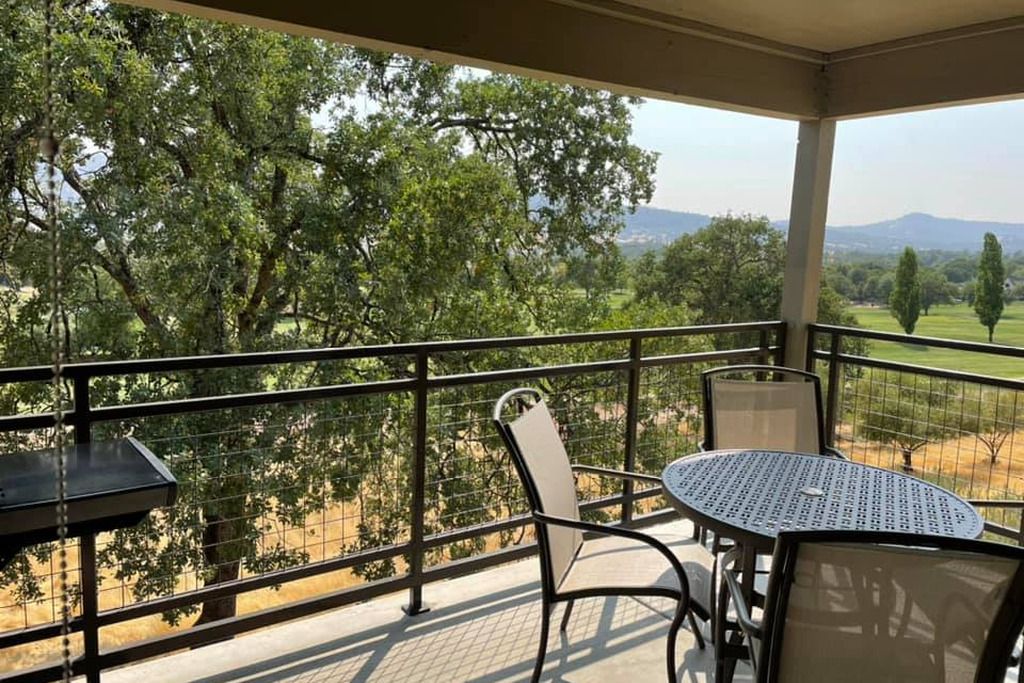 A balcony with a table and chairs, overlooking a landscape with trees and distant hills.