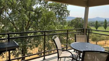 A balcony with a table and chairs, overlooking a landscape with trees and distant hills.