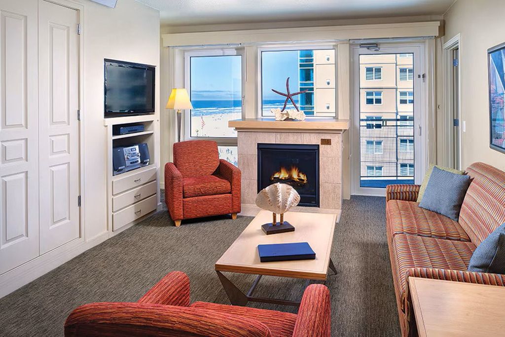 A living room with a fireplace, a television, and a view of the beach.