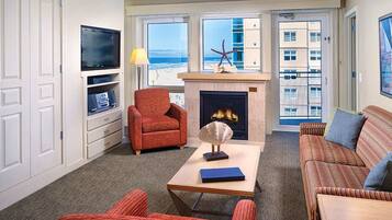 A living room with a fireplace, a television, and a view of the beach.