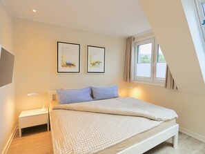 A bedroom with a bed, a nightstand, a window, and two framed pictures on the wall. - 214 - Apartment 14 "blue Anchor" (Juist)