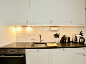 A modern kitchen with white cabinets, a stainless steel sink, and a built-in oven. - 214 - Apartment 14 "blue Anchor" (Juist)
