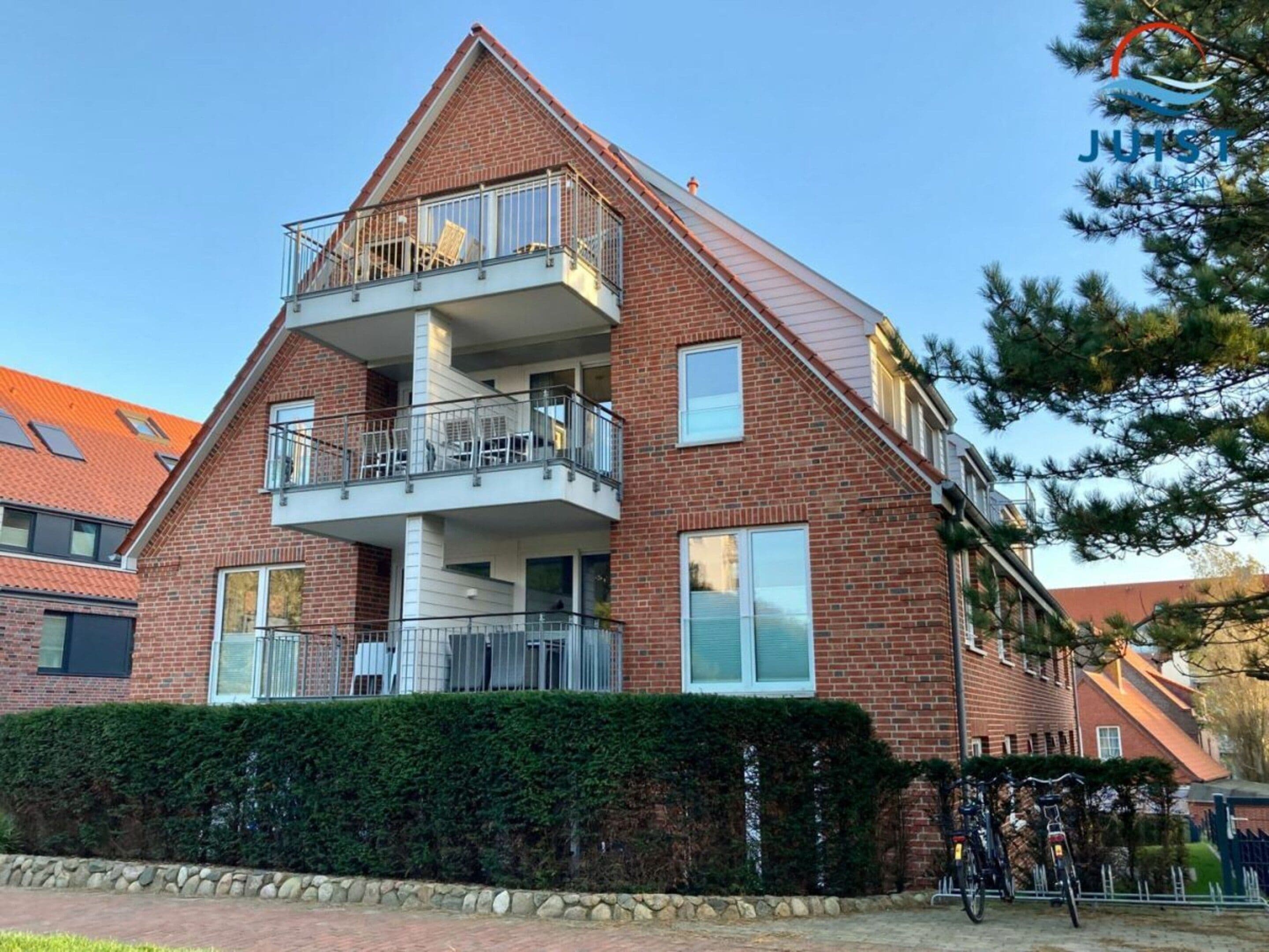 A two-story residential building with a balcony on the upper floor, a stone wall in front, and bicycles parked outside.