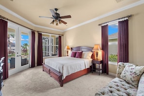 Une chambre à coucher comprenant un lit, une table de chevet, une lampe, un ventilateur de plafond et une vue sur l’extérieur.
